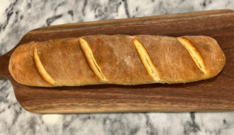 baguette recipe full loaf golden crust on a wooden cutting board